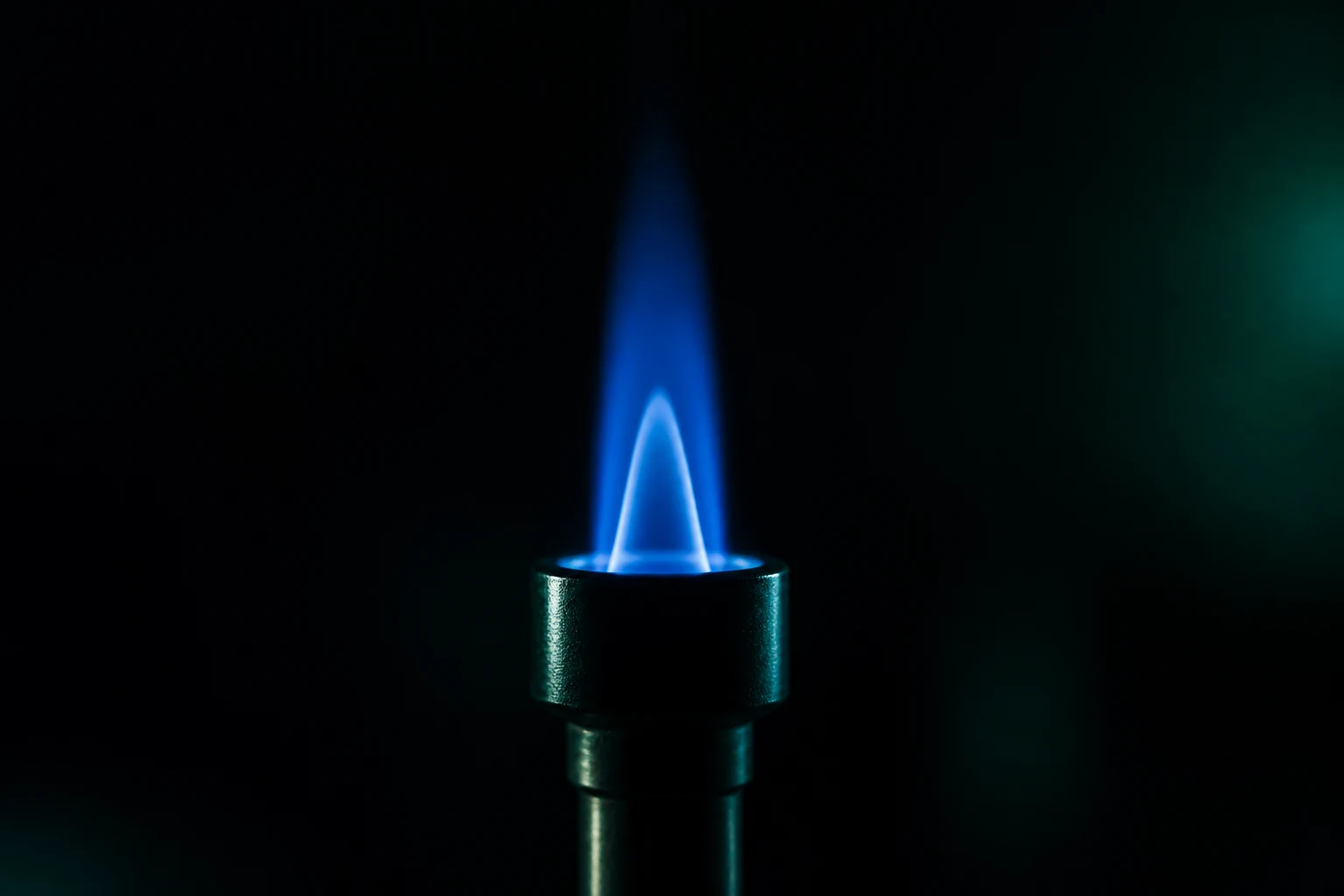 Chama pequena e estável de queimador de laboratório em ambiente escuro, com o cone azul nítido no centro